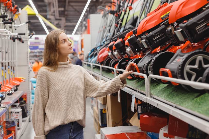 A woman shops and looks at a lawnmower she may want to buy.
